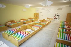 a room filled with lots of wooden beds and rainbow colored sheets on top of them