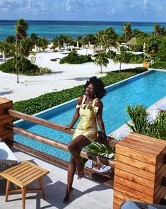 a woman in a yellow dress sitting on a balcony next to a pool and beach