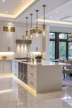 a large kitchen with white cabinets and marble counter tops is lit by pendant lights that hang from the ceiling