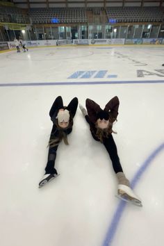 two people are laying on the ice with their legs spread out and one person is holding an object