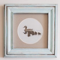 a duck and her chicks in a blue frame hanging on the wall next to a white wall