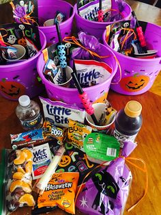 purple buckets filled with halloween candy and candies sitting on a wooden table top