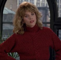 a woman with blonde hair wearing a red turtle neck sweater in front of a window