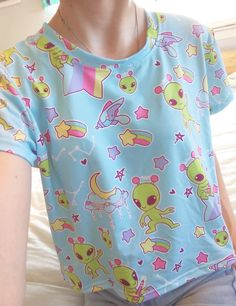 A pastel blue alien shirt featuring little green aliens who are only out to abduct your heart and bring a little shock of pastel to your life. This cropped t-shirt, which has a slightly silky, knit feel, also has contrasting rainbows and stars. It's unisex and fits loose, making for a comfy casual addition to your fairy kei and decora wardrobe while being low-key. Apparel and bedding ship separate from handmade items. Delivered in 2-4 weeks. The colors print more pastel than the items I make mys Light Blue Kawaii, Wardrobe Overhaul, Alien Clothes, Pastel Goth Outfits, Blue Alien, Alien Shirt, Bright Outfits, Alien Aesthetic, Kawaii Fairy