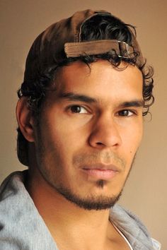 a young man with curly hair and a hat on his head looking at the camera