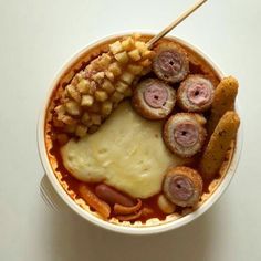 a bowl filled with meat and potatoes on top of a white table next to a wooden spoon