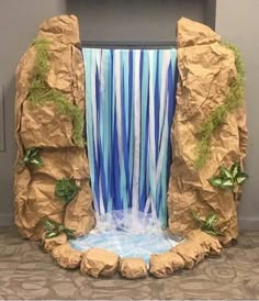 a waterfall made out of brown paper with blue streamers and green plants on it