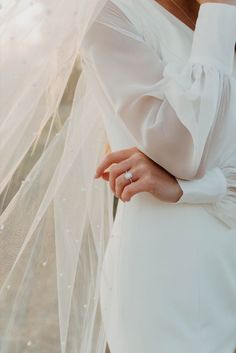 a woman wearing a wedding dress and veil with her hand on the back of her shoulder