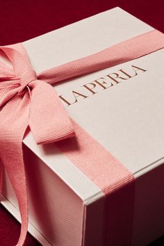 a box with a pink ribbon tied around it on a red tableclothed surface