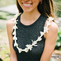 a woman wearing a necklace with white flowers on it and smiling at the camera while standing outside