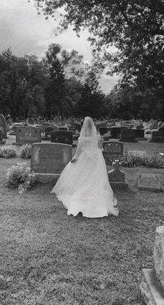 a woman in a wedding dress walking through a cemetery