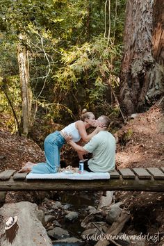 a man and woman kissing on a bridge in the woods