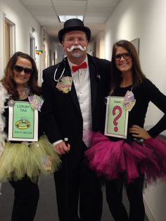 two women and a man in tutus are posing for the camera while holding signs with question marks on them