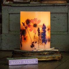 a lit candle sitting on top of a wooden table next to a book with flowers painted on it