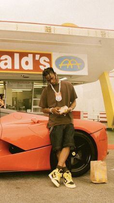 a man sitting on the hood of an orange sports car in front of a store