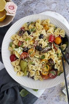 a white bowl filled with pasta salad next to a cup of lemonade and two black chopsticks