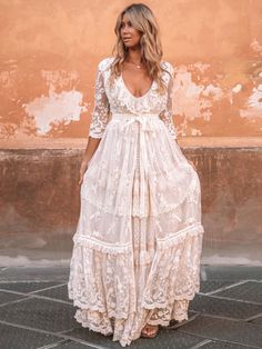 a woman standing in front of a wall wearing a white dress with lace on it