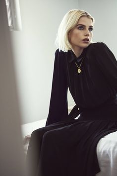 a woman sitting on top of a bed wearing a black dress