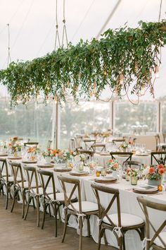 the tables are set up with white linens and greenery hanging from the ceiling