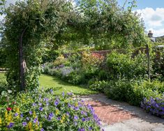 the garden is full of colorful flowers and plants, including an arch in the middle