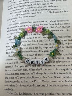 an open book with a bracelet made out of beads and letters that spell the word betty