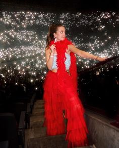 a woman in a red dress is standing on some steps with her arms out to the side