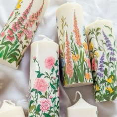 four candles with flowers painted on them sitting on a white sheet next to other items