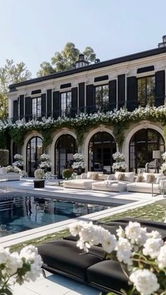 an outdoor swimming pool in front of a large house with white flowers on the lawn