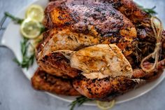 a roasted chicken on a plate with lemons and herbs