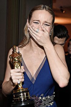 a woman covers her face with her hands as she holds an oscar statue in front of her