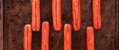 several hot dogs are lined up on a metal tray, ready to be grilled