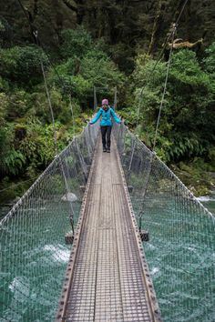 a person walking across a suspension bridge in the middle of a river with trees on both sides