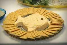 crackers arranged in the shape of a fish on a plate next to a bowl of dip