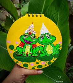 two green frogs with hats on their heads sitting next to each other in front of leaves