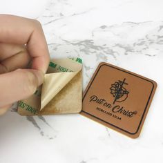 a hand is holding a piece of paper next to a small square coaster on a marble surface