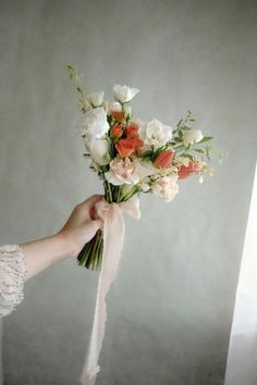 a person holding a bouquet of flowers in their hand with a ribbon around the wrist