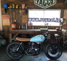 the motorcycle is parked in the garage by the table and shelves with tools on it