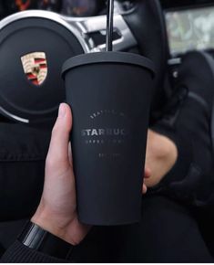 a person holding a cup with a straw in their hand and steering wheel behind them