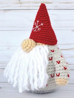 a crocheted gnome with a red hat and white beard sitting on top of a wooden table