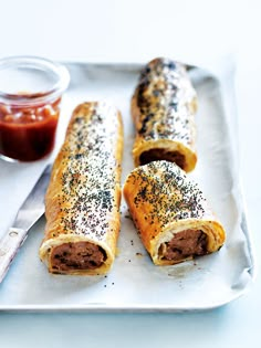 two sausage wrapped in bread on a white plate next to a jar of ketchup