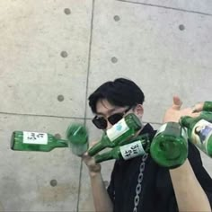 a man is holding up several empty green bottles