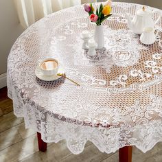 a white lace tablecloth on a wooden table with flowers in vases and cups