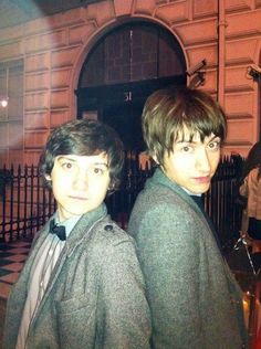 two young men standing next to each other in front of a building with an iron fence