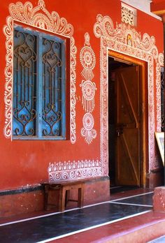 an orange building with ornate designs painted on the walls and windows, along with a wooden bench