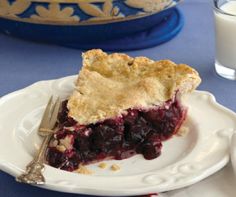 a piece of pie on a plate with a fork and glass of milk next to it