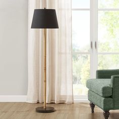 a living room with a green chair and a lamp on the floor in front of a window