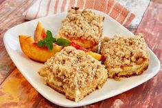 a white plate topped with four pieces of cake next to peaches and strawberries