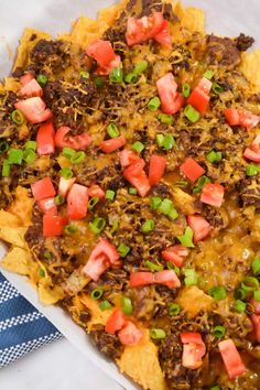 nachos with beef, cheese and tomatoes on top in a white dish next to a blue napkin