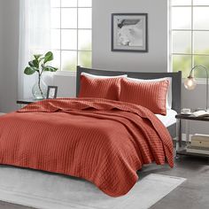 a bed with an orange bedspread in a room next to a table and window