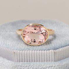 a ring with an oval cut pink topazte sits on a white cloth covered box